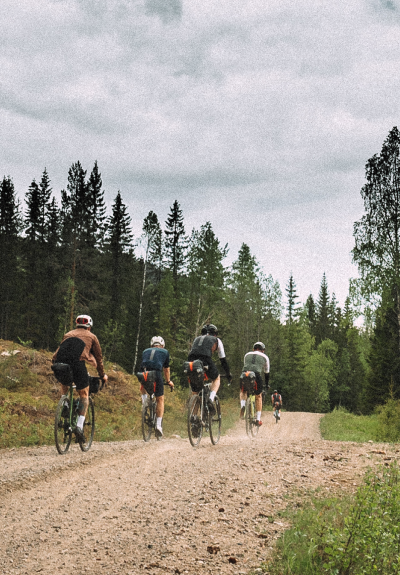 Five cyclists gravel riding away from camera in dense forest