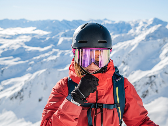 Female athlete in googles backcountry skiing black helmet red jacket